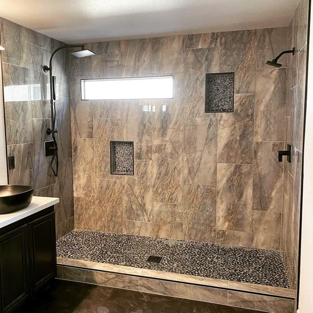 Double-head walk-in shower with large stone-look porcelain tile, recessed niches and a pebble shower floor