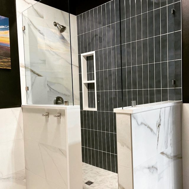Shower with charcoal vertical stacked tile, marble-look half walls and a recessed niche